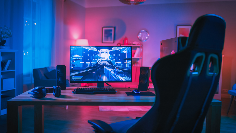 Powerful Personal Computer Gamer Rig with First-Person Shooter Game on Screen. Monitor Stands on the Table at Home. Cozy Room with Modern Design is Lit with Pink Neon Light