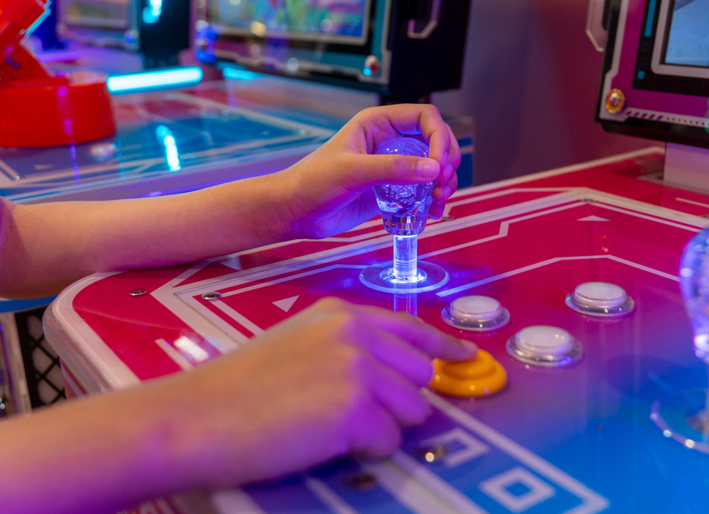 A person's hands gripping a joystick and pressing buttons on an arcade game machine. Nostalgia, fun, and entertainment from classic arcade gaming concept