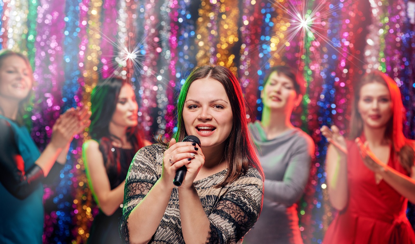Happy best girlfriends having fun together applauding a friend who is singing karaoke