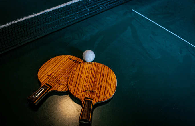 A pair of rackets with a ping pong ball lying on a table