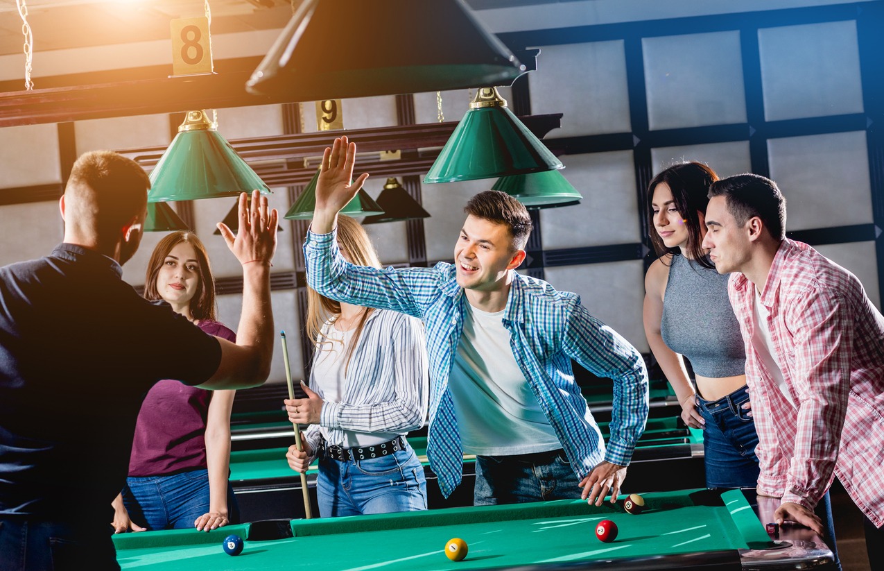 A group of friends celebrating a good shot over the billiards table
