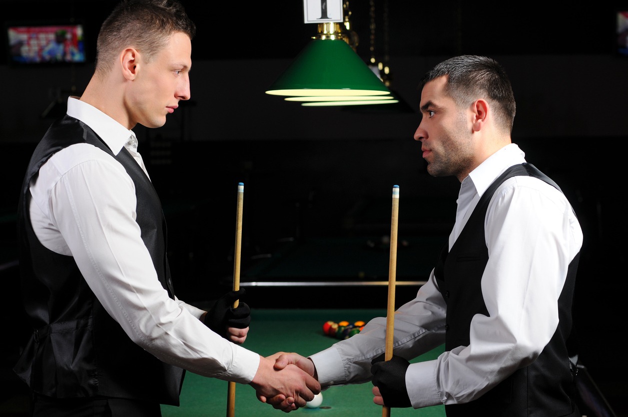 Two players shaking hands in front of a billiards table before a competitive match