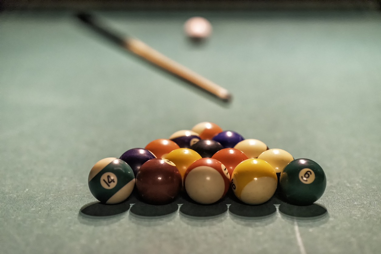 billiard balls, cue ball and cue stick set atop a table ready for a game to begin