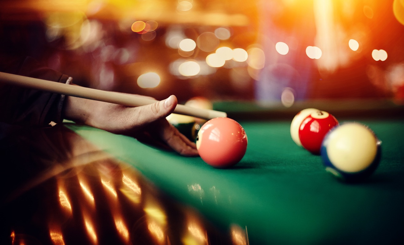 close-up photo of a player’s hand preparing to take a shot at a billiards table